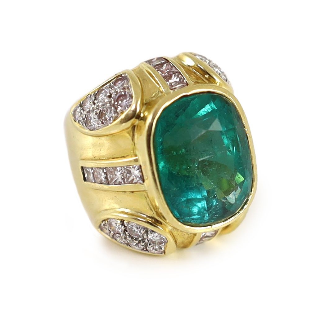 A large gold and single stone oval cut emerald set dress ring, with round and princess cut diamond cluster set shoulders